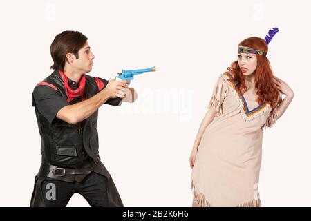 Giovane cowboy che punta la pistola alla donna in costume vecchio stile su sfondo grigio Foto Stock