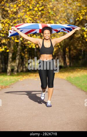 Felice giovane jogger femmina che tiene la bandiera britannica sul percorso nel parco Foto Stock