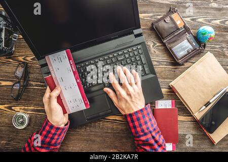 Prepararsi per un viaggio emozionante. L'uomo prenota i voli digitando su un computer portatile e pagando con una carta di credito su uno sfondo di legno. La vista dall'alto Foto Stock