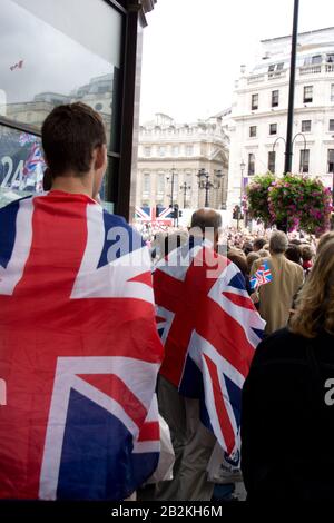 Due uomini visti dalla parte posteriore drappeggiato in bandiere dell'Unione, Unions jacks a Londra , Inghilterra Foto Stock