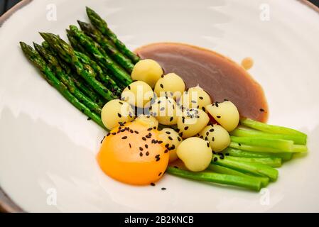 Asparagi con patate novelle, con salsa di carne e tuorlo d'uovo su un piatto Foto Stock
