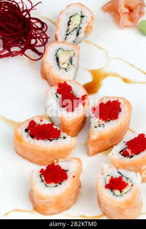Primo piano di diversi sushi roll disposti su un piatto bianco. I panini sono avvolti nel salmone e ripieni di riso, cetriolo e altri ingredienti. Alcuni rotoli sono ricoperti da caviale rosso brillante. Il Foto Stock