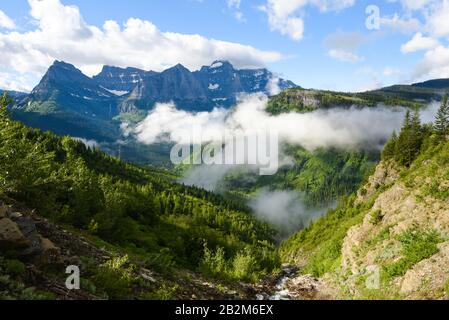 Sopra le nuvole che si affacciano su una valle nel Glacier National Park con pini, fiume e lontano Foto Stock