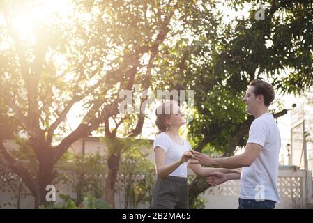 Felice coppia amorevole abbracciando e ballando all'aperto in estate sotto l'ombra dell'albero.giovane uomo e donna caucasica danza nel cortile Foto Stock