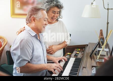 Anziano anziano uomo suona piano in casa di cura ascoltato da donna anziana, ritrattamento anziani nonna asiatica e nonno suonare piano in casa Foto Stock