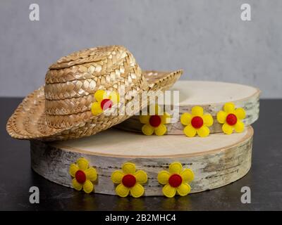 Cappello di paglia sulla cima di elementi di legno di betulla decorato con fiori gialli con centri rosa scuro seduti contro una ardesia nera e backgroun intonaco Foto Stock