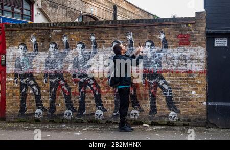 Un uomo prende una foto di un pezzo di arte graffiti che mostra 5 calciatori ed è perfettamente allineato con una delle figure dipinte. Foto Stock