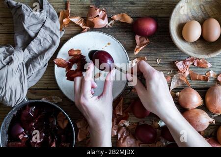 Donna che fa tinto uova di Pasqua dipinte con cipolla colorante naturale su sfondo di legno. Processo di tintura delle uova con vernici naturali per Pasqua. ecol naturale Foto Stock