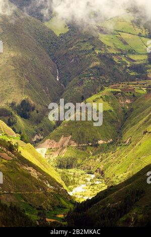 Una vista ad alto angolo di una valle di montagna profonda e verdeggiante con ripidi pendii ricoperti di erba. Un tortuoso fiume scorre attraverso il fondovalle, circondato da macchie di alberi e terreni coltivati. Un magro Foto Stock