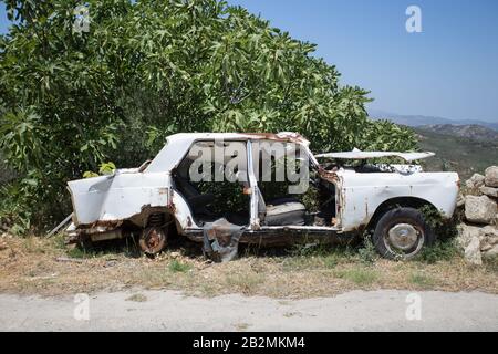 un'auto vecchia, arrugginita e distrutta si distrugge sotto un albero, senza porte e finestre. Isola di Creta, Grecia Foto Stock