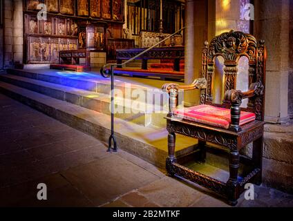 Antica sedia in legno nell'interno illuminato al sole dell'Abbazia di Hexham. Il vetro colorato di Sunshine thuf causa i modelli appled di luce colorata sui gradini della pietra. Foto Stock