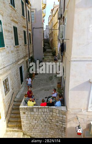 Persone sedute in una stretta strada laterale nel centro storico, Dubrovnik, Croazia Foto Stock