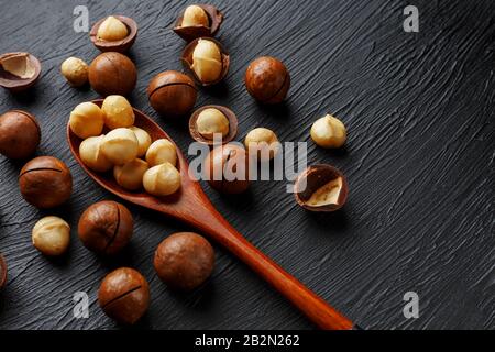 Noce macadamia sgusciata e noce macadamia sbucciata su sfondo di tessitura nera. Il dado più costoso del mondo, in crescita in Australia. Vista dall'alto e. Foto Stock