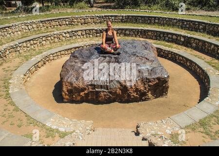 il meteorite più grande del mondo a Grootfontein, Namibia. Un pezzo enorme di ferro dallo spazio. Ragazza bianca turista seduto su un meteorite Foto Stock