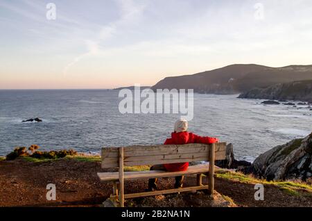 Uomo che si rilassa su una panchina woden a Loiba Cliffs, Ortigueira, Spagna Foto Stock