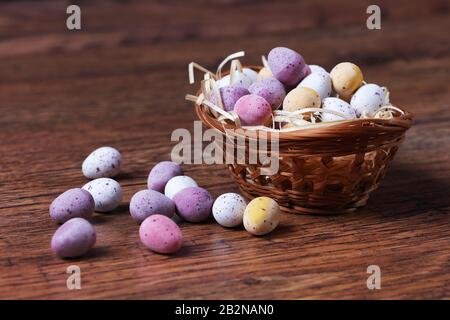 Un primo piano imamge di uova di caramella di Pasqua in un cesto con paglia su tavola di legno con fuoco selettivo e profondità di campo poco profonda Foto Stock