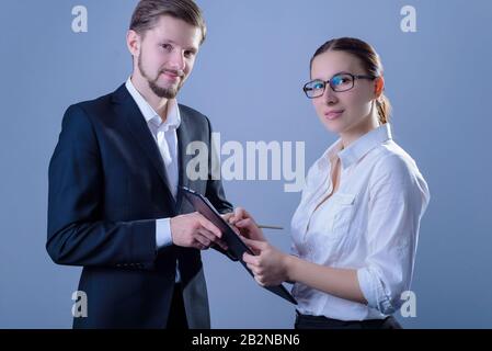 ritratto di due giovani uomini d'affari, in abiti d'affari, una donna d'affari tiene una cartella nella sua mano in modo che l'uomo d'affari segni. Studio foto su un g Foto Stock