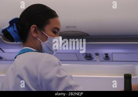 Una stewardess dell'aria della Bangkok Airways che indossa una maschera facciale mentre serve le bevande durante l'epidemia di Coronavirus su un volo tra Bangkok e Phnom Penh. Foto Stock