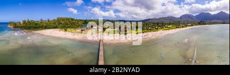 Immagine panoramica aerea al largo della costa sulla Baia di Hanalei e molo sull'isola hawaiana di Kauai con surfisti in acqua Foto Stock