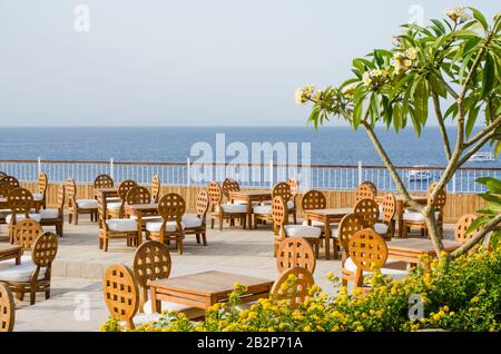Tavoli e sedie in legno sulla terrazza di un accogliente caffè estivo con vista sul mare. Giornata estiva soleggiata vicino al mare. L'esterno del caffè o del ristorante. Foto Stock