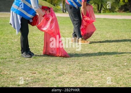 Uomo e donna che indossa volontario di prelevare i rifiuti e i rifiuti plastici in parco pubblico. Giovani indossando i guanti e la messa per lettiera in rosso il sacchetto in plastica Foto Stock