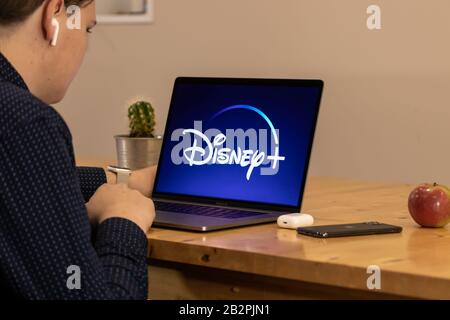 Uomo seduto su un ponte che guarda il logo Disney Plus, il nuovo servizio di streaming di Disney. Foto Stock