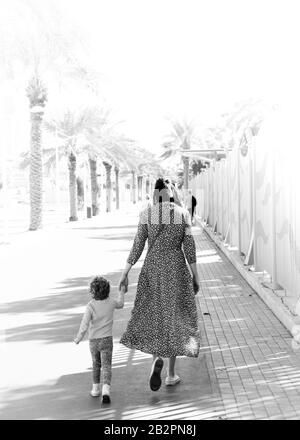 Madre e bambino camminano mano in mano lungo passerella costeggiata da palme in bianco e nero Foto Stock