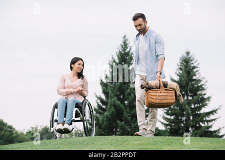 bell'uomo che tiene il cesto di paglia vicino alla ragazza disabile nel parco Foto Stock