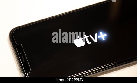 IPhone con il logo Apple TV + (Plus) sullo schermo quando è posizionato su un tavolo bianco. Foto Stock