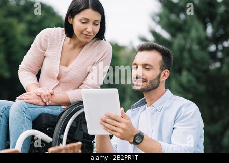 felice donna disabile e ragazzo sorridente utilizzando il tablet digitale nel parco Foto Stock