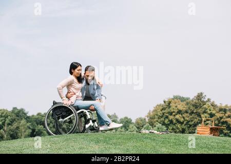 bel giovane uomo che prende giovane ragazza disabile dalla sedia a rotelle Foto Stock