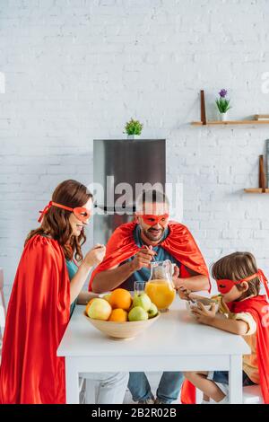 famiglia in costumi di supereroi che hanno colazione in cucina insieme Foto Stock