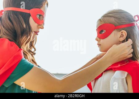 vista laterale della donna e adorabile figlia in costumi di supereroi che si guardano l'uno all'altro Foto Stock