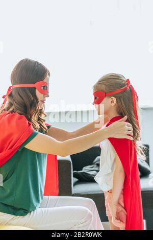 madre e figlia in costumi di supereroi che si guardano a casa Foto Stock