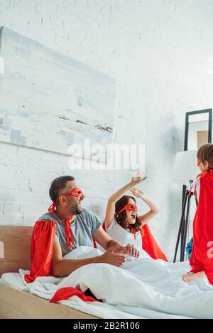 buona famiglia in costumi di supereroi divertirsi a letto al mattino Foto Stock