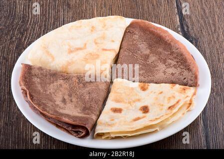 I pancake sono semplici e con cacao. Pancake su un piatto bianco su uno sfondo di legno. Colazione tradizionale russa. Foto Stock