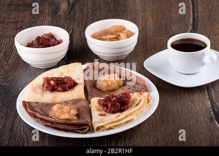 I pancake sono semplici e con cacao. Frittelle su un piatto bianco, marmellata di mele di diverse varietà e caffè su uno sfondo di legno. Russia Tradizionale Foto Stock