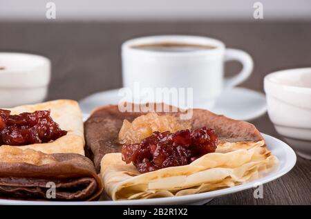 Messa a fuoco selettiva. I pancake sono semplici e con cacao. Frittelle su un piatto bianco, marmellata di mele di diverse varietà e caffè su uno sfondo di legno. T Foto Stock