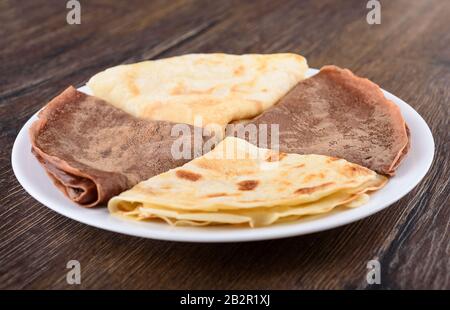 Messa a fuoco selettiva. I pancake sono semplici e con cacao. Pancake su un piatto bianco su uno sfondo di legno. Colazione tradizionale russa. Foto Stock