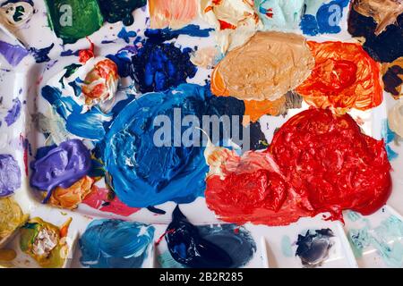 Bella colorata vernici a trama dello sfondo. Pennellate di vernice e left overs di residui di vernici in tavolozza di colori schiera sul tavolo. Macchie colorate e blo Foto Stock