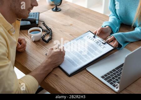 vista ritagliata del contratto di firma manuale negli appunti in agente di viaggio Foto Stock