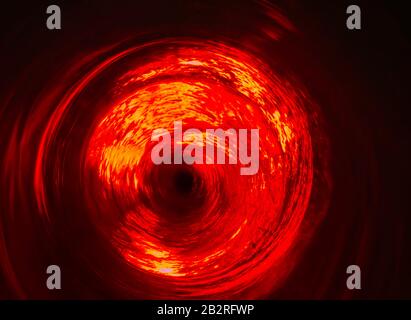 Un ciclone d'acqua rosso illuminato in un imbuto di vetro Foto Stock