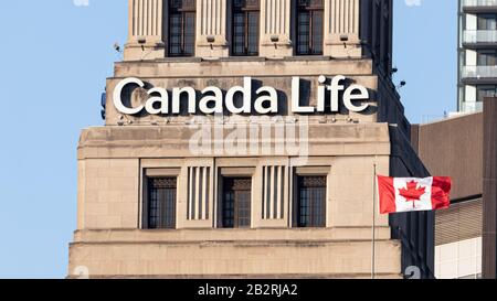 Canada Life segno in cima alla loro sede principale a Toronto con una bandiera canadese visto ondeggiante di fronte. Foto Stock