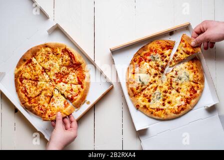 Prelievo di fette di pizza da scatole di cartone. Pizza Margherita e quattro formati. Pizza in una scatola di consegna Foto Stock