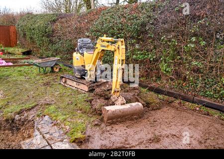 Cardiff, GALLES - GENNAIO 2020: Mini escavatore scavando il prato nel giardino posteriore di una proprietà residenziale Foto Stock