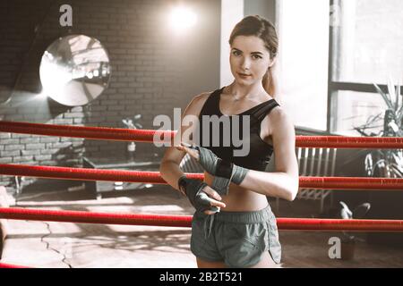 Giovane bella boxer ragazza tira bandage prima della lotta o l'allenamento in boxing anello. Pugilato Fighter Preparazione Di Bende Per L'Allenamento Foto Stock