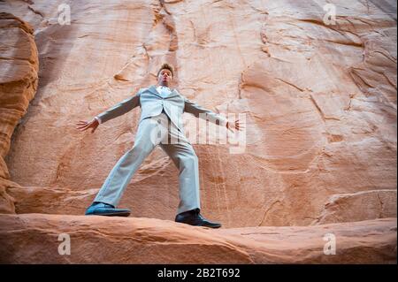 Uomo d'affari nervoso equilibrio su una stretta sporgenza in un canyon di roccia rossa Foto Stock