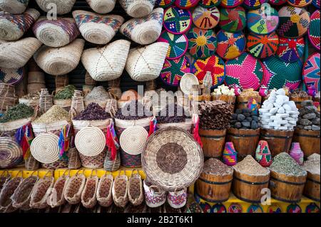 Colorati cesti e borse tessuti appendere sopra tumuli di spezie ed erbe in una stalla di mercato nel souk ad Assuan, Egitto Foto Stock