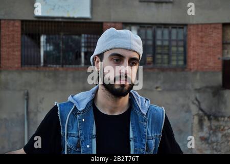 Un uomo triste che indossa berretto e guarda in basso/ un uomo che sale di fronte a un vecchio edificio Foto Stock