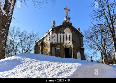 Montreal Quebec Canada 1 marzo 2020: Vecchio mausoleo con terreno innevato su cielo blu giorno soleggiato, Mount Royal Cemetery Foto Stock